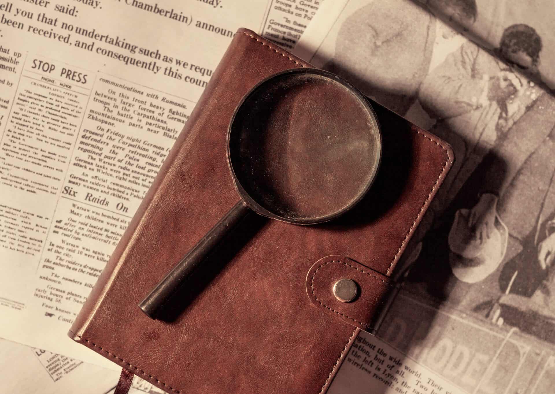 A magnifying glass placed on top of a leather bound notebook over old newspaper.