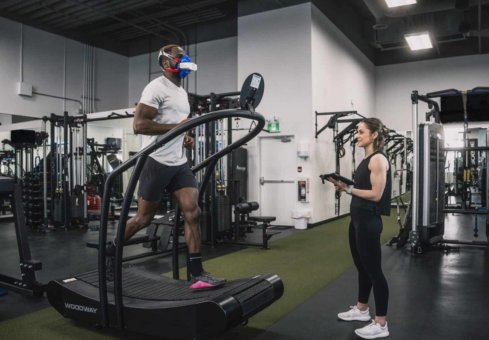 Female trainer recording performance data while a man runs on a treadmill with the VO2 Master analyzer and mask